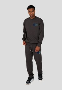 Felpa grigia scura e pantaloni jogger coordinati, con testo blu "WRONG FRIENDS" sul petto e sulla gamba. Sneakers nere con dettagli grigi.