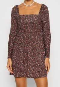 Robe noire à fleurs avec des manches longues, décolleté carré et taille froncée, présentant de petits motifs de fleurs roses et bleues.