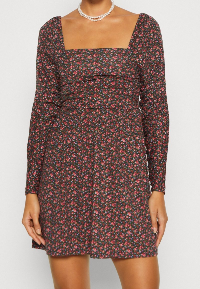 Robe noire à fleurs avec des manches longues, décolleté carré et taille froncée, présentant de petits motifs de fleurs roses et bleues.