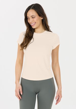 Lichtbeige aansluitend T-shirt met korte mouwen en een ronde halslijn, gedragen met een donkere groene legging, gemaakt van een gladde, rekbare stof.