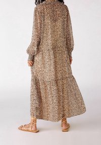 Abito lungo a più strati in tessuto trasparente color tan con stampa leopardata nera e marrone. Presenta maniche a sbuffo e polsini elasticizzati. Abbinato a sandali flat.