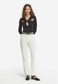 Svart långärmad bodysuit med utskärningar, i kombination med vita raka jeans och svarta sandaletter med remmar. Enkel bälte framhäver midjan.