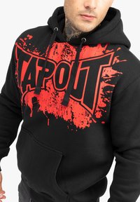 Melnā sporta krekls ar lielu sarkanu "TAPOUT" grafiku, splatter dizainu, ar auklu regulējamu kapuci un priekšējo kangaru kabatu. Strukturēta auduma.