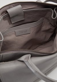 Sac à main en cuir gris ouvert montrant une doublure intérieure en tissu doux, une poche intérieure zippée et une étiquette de marque "ZIGN".