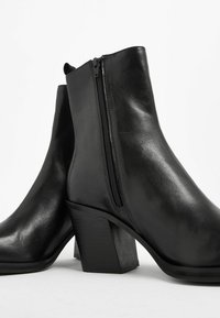 Stivali ankle in pelle nera con tacco a blocco rettangolare, zip laterale e texture liscia, caratterizzati da un design minimalista.