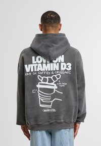 Szara, oversize bluza z kapturem z dużym nadrukiem z tyłu, zawierającym białe teksty oraz ilustracje kawy i wypieku, wykonana z materiału bawełnianego.