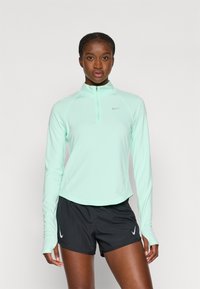 Lys myntegrønn langermet treningstopp med kvart glidelås og grå Nike-logo, kombinert med svarte shorts med hvit Nike-logo.