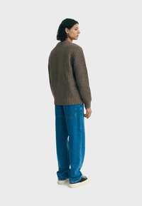 Un pull en tricot côtelé marron avec un col rond, associé à un pantalon en denim bleu évasé et des chaussures crème, vu de dos.