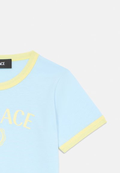 Ανοιχτό μπλε βαμβακερό μπλουζάκι με κίτρινο ριγέ γιακά και μανίκια; διαθέτει εκτύπωση "ACE" σε κίτρινο με διακοσμητικές λεπτομέρειες από κάτω.