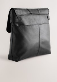 Sac à main en cuir noir avec rabat pliant et coutures apparentes, présenté sur un fond clair uni.