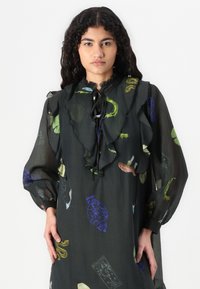 Robe en chiffon noir avec col volanté, manches longues et lien à cordon. Présente des motifs colorés d'animaux et de vaisseaux tout au long.