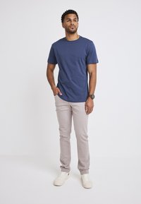 Mörkblå kortärmad t-shirt i kombination med ljusbeige slim-fit byxor och vita sneakers, stående mot en helt vit bakgrund.