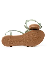 Sandalia de cuero verde con tiras finas y un pequeño tacón cuadrado. La suela presenta un patrón de rosas y la grabación "Hecho en España". Diseño antideslizante.