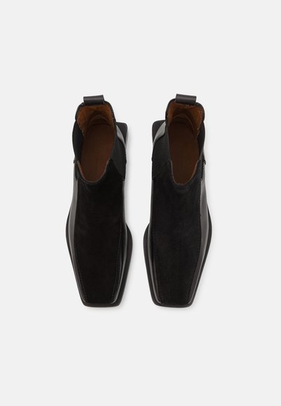 Bottines en cuir noir et en daim, avec un bout pointu, une semelle plate et un design classique. Équipées d'une languette pour un enfilage facile.