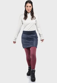 Weißes langärmliges Oberteil mit Reißverschluss, marineblaue isolierte Rock, rote Leggings und schwarze Wanderstiefel, entworfen für Outdoor-Aktivitäten.