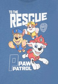 Blå t-skjorte med tegneseriekjæledyr fra "Paw Patrol." Teksten sier "TIL REDNING" og "PAW PATROL." Hunder er fargerike med distinkte antrekk.