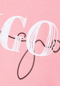 Gros plan sur les lettres stylisées blanches et noires "GO" imprimées sur un tissu rose texturé.