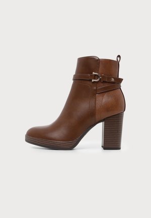 Brauner Lederknöchel-Stiefel mit strukturierter Rückseite, dekorativem Riemen und Schnalle sowie gestapeltem Blockabsatz auf weißem Hintergrund.