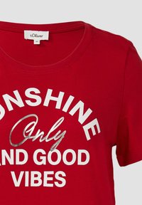 Rode katoenen T-shirt met een ronde hals en witte en zilveren bedrukte tekst: "SUNSHINE Only AND GOOD VIBES." Korte mouwen.