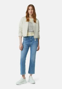 Lichtbeige gewatteerde bomberjack over een gemêleerd cropped top en lichtblauwe rechtlopende jeans, gecombineerd met witte sneakers.