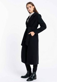 Czarny długi płaszcz z taliowaniem i bocznymi kieszeniami, wykonany z gładkiego materiału. Posiada wycięty kołnierz oraz pasek w talii.