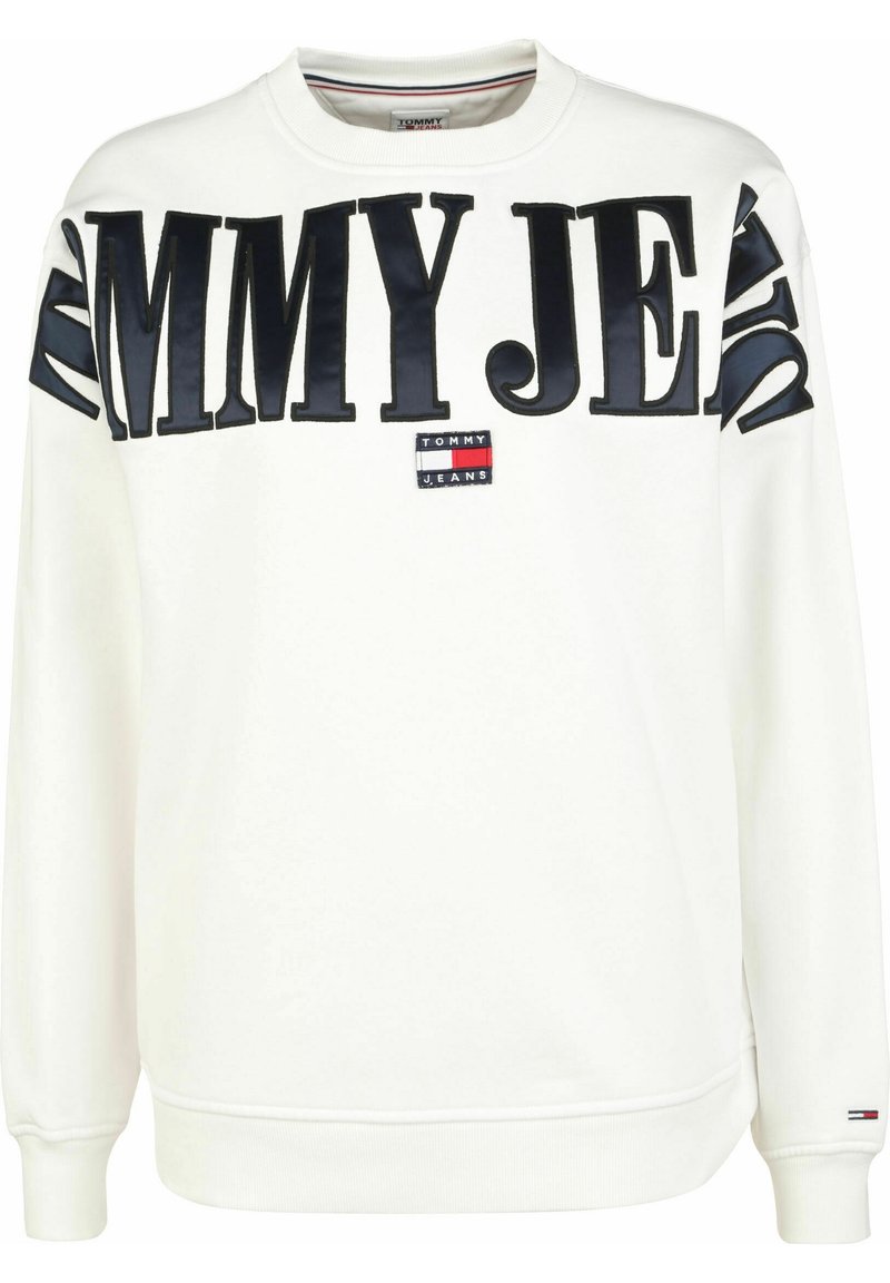 Vit sweatshirt gjord av mjukt material, med djärv svart "TOMMY JEANS" text och ett litet logopatch i röd, vit och blå.