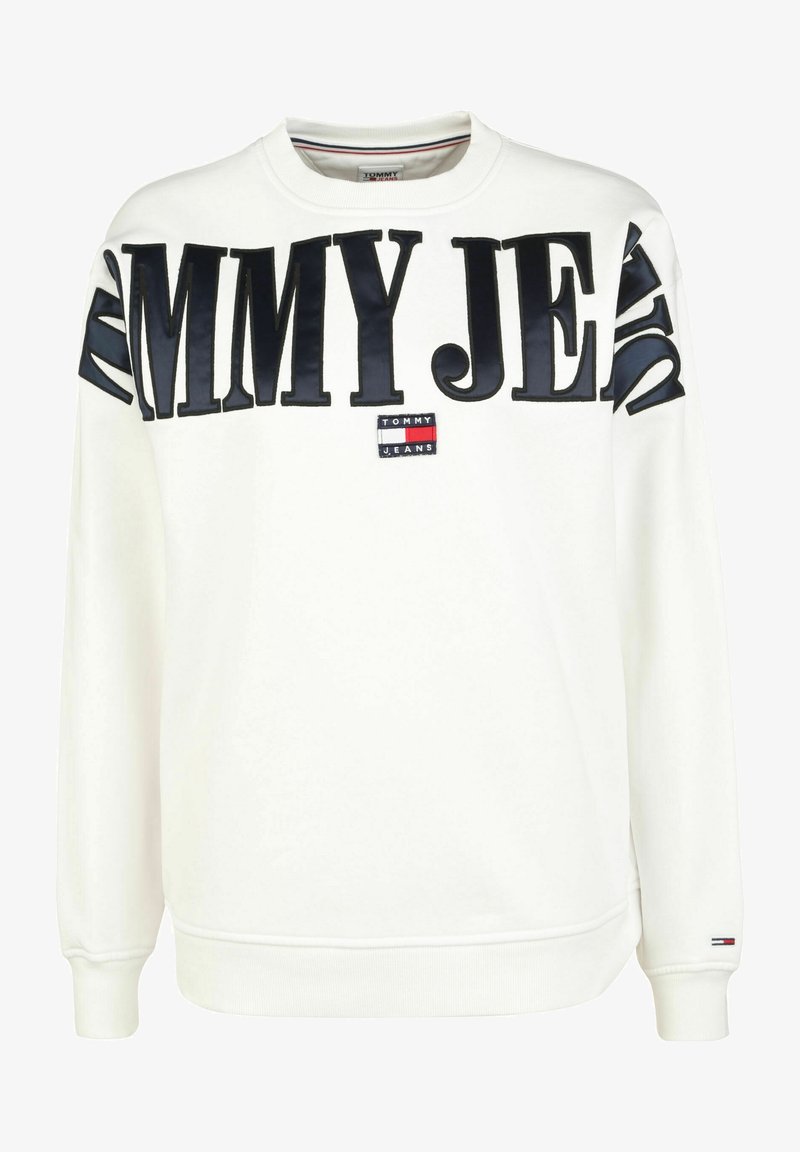 Vit sweatshirt gjord av mjukt material, med djärv svart "TOMMY JEANS" text och ett litet logopatch i röd, vit och blå.