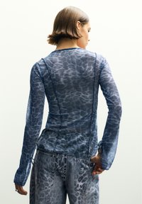 Plava, strukturirana majica dugih rukava s suptilnim uzorkom životinja, u kombinaciji s svijetloplavim trapericama s uzorkom koje imaju stražnje džepove i bočne kravate.