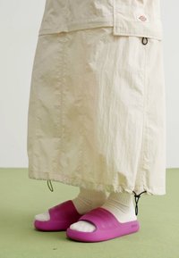 Beige, knälång regnkjol med rynkad nederkant, matchad med rosa gummisandaler och vita ankelsockor. Minimalistisk design med en avslappnad stil.
