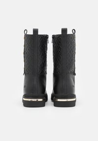 Bottines noires avec un panneau texturé, des accents dorés sur les semelles et des fermetures éclair latérales. Talon renforcé pour un soutien accru.