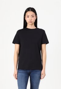 Black short-sleeve t-shirt made of cotton, featuring a classic crew neck and a relaxed fit. Worn with blue jeans.