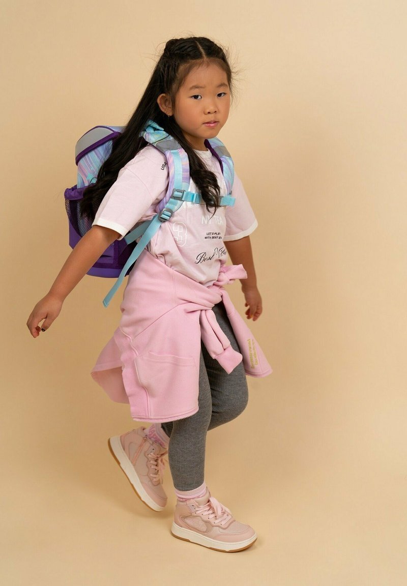 Lila und blaue Tasche, pinkes T-Shirt, pinker Pullover um die Taille gebunden, graue Leggings und hellpinke Turnschuhe. Einheitliche Farben und verschiedene Texturen.