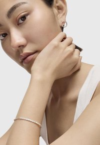 Orecchini a cerchio in argento e un delicato bracciale in argento con accenti circolari, indossati da una persona con pelle liscia, su uno sfondo neutro.