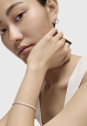 Orecchini a cerchio in argento e un delicato bracciale in argento con accenti circolari, indossati da una persona con pelle liscia, su uno sfondo neutro.
