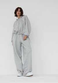 Szara, oversize'owa bluza z kapturem na zamek i sznurkiem, w komplecie z luźnymi spodniami dresowymi w tym samym kolorze. Obie części mają miękkie, teksturowane wykończenie.