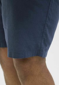 Marineblaue Baumwollshorts mit glatter Textur, einem geraden Saum und minimalem Nähdetail am Boden.