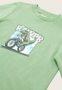 Zelená mikina s okrúhlym výstrihom, na ktorej je grafika dinosaura jazdiaceho na bicykli, doplnená textom "RAWRR" v tučných písmach.