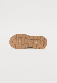 Semelle de chaussure en caoutchouc marron avec des rainures profondes et deux petits trous circulaires visibles sur un fond blanc uni.