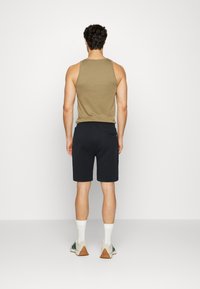 Olive green tank top paired with dark navy shorts. The shorts have a back pocket. White ankle socks and green-accented sneakers complete the outfit.