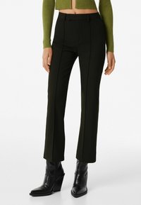 Tummanvihreät räätälöidyt housut kapealla istuvuudella, joissa on etukäytävät ja sileä pinta. Yhdistetty mustiin teksturoituihin korkokenkiin.