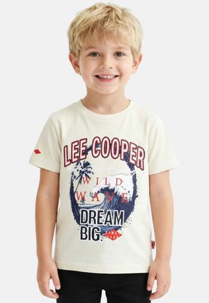 Jeune garçon blond portant un t-shirt blanc "Lee Cooper" avec un graphisme de vague et les textes "Wild Wave" et "Dream Big".