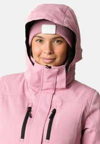 Giacca isolante rosa chiaro con colletto alto, cappuccio regolabile e due tasche frontali con zip. Berretto lavorato a maglia rosa.