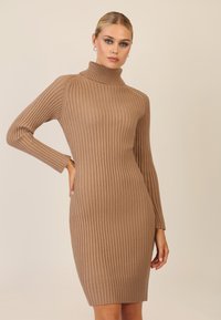 Strikket turtleneck kjole i lys brun; fremhæver lodret ribbemønster, lange ærmer, tætsiddende silhuet og længde til midt på låret.
