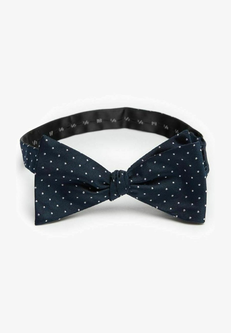 Mörkblå fluga med vita prickar, tillverkad av texturerat tyg, med en knuten mittdel och justerbar svart rem.