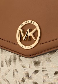 Brun lædertaske med et guldtonet cirkulært logo med "MK." Beige mønstret stof med et subtilt logodesign på fronten.