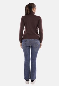 Maglione a collo alto marrone con maniche aderenti, abbinato a jeans a zampa d'elefante blu e sneakers bianche, visto da dietro.
