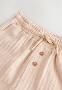 Pantalons élastiques rose clair avec taille ajustable, dotés de deux boutons marron et d'un tissu texturé en côtes.