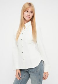 Valge teksasärk kraega kaelusega, pikkade varrukatega ja esitaskute nööpidega. Särgile on lisatud üks rindtasku ja kergelt kaarduv ääreosa.