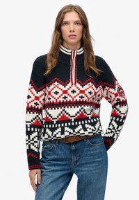 Gebreide pullover met een hoge kraag, voorzien van een geometrisch patroon in marineblauw, wit en rood. Soepele textuur en geribbelde manchetten.