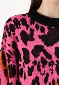 Jersey de punto con un diseño de estampado de leopardo en negro y rosa, con un cuello de canalé negro y acentos naranjas en las mangas.
